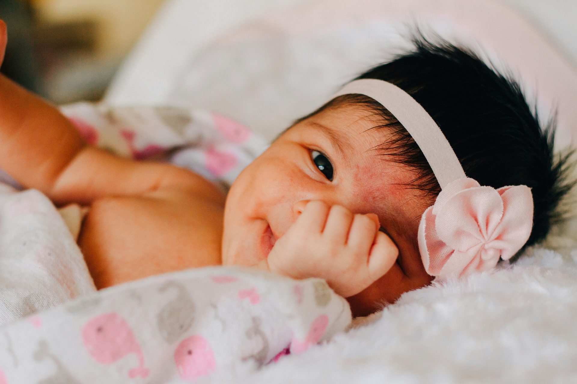 baby wearing white floral headband lying on bed while smiling