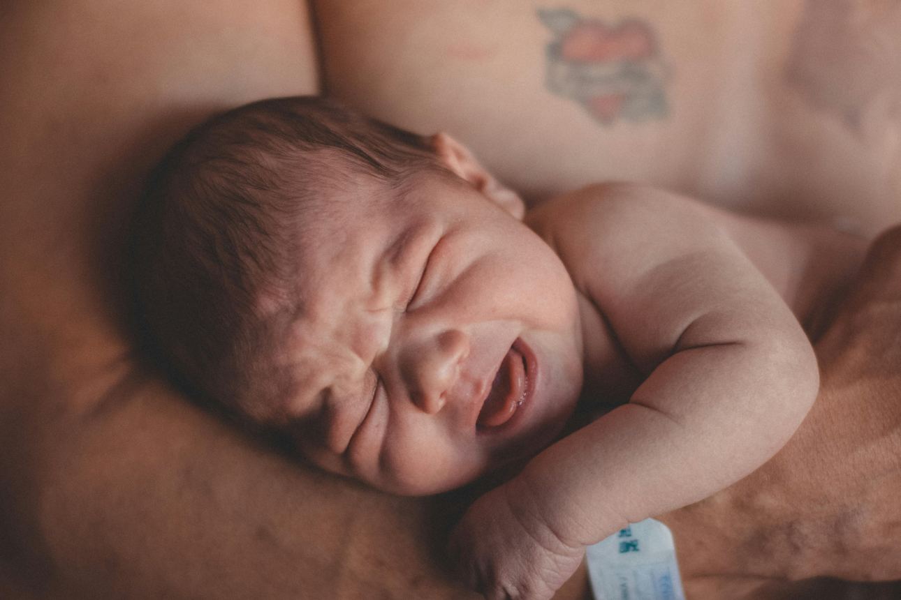 A mother smiles lovingly at her newborn in a hospital delivery room, attended by medical staff.